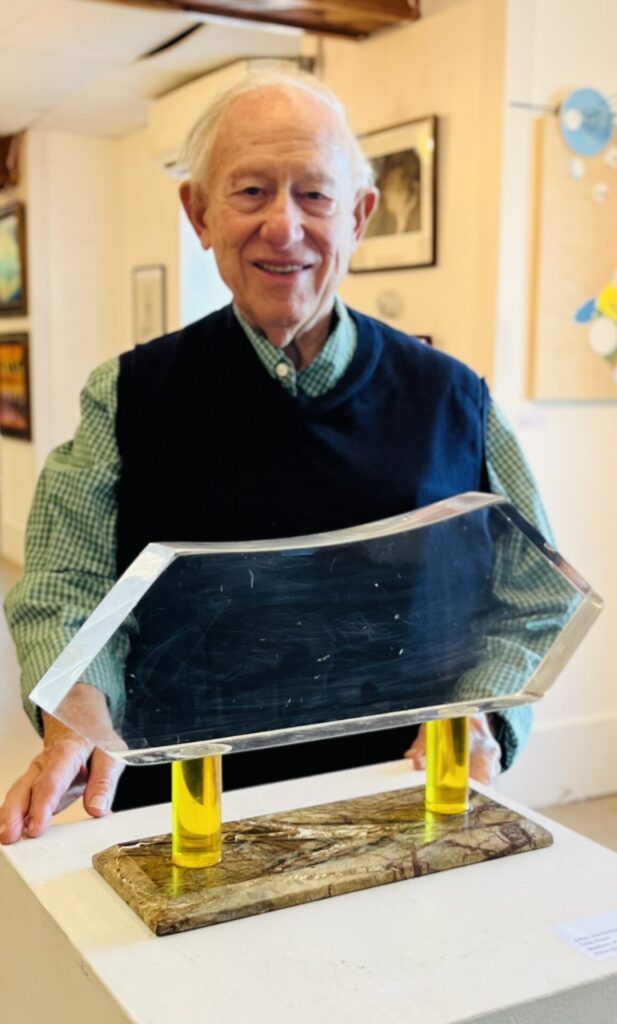 photo of older man smiling with plexiglas sculpture he created